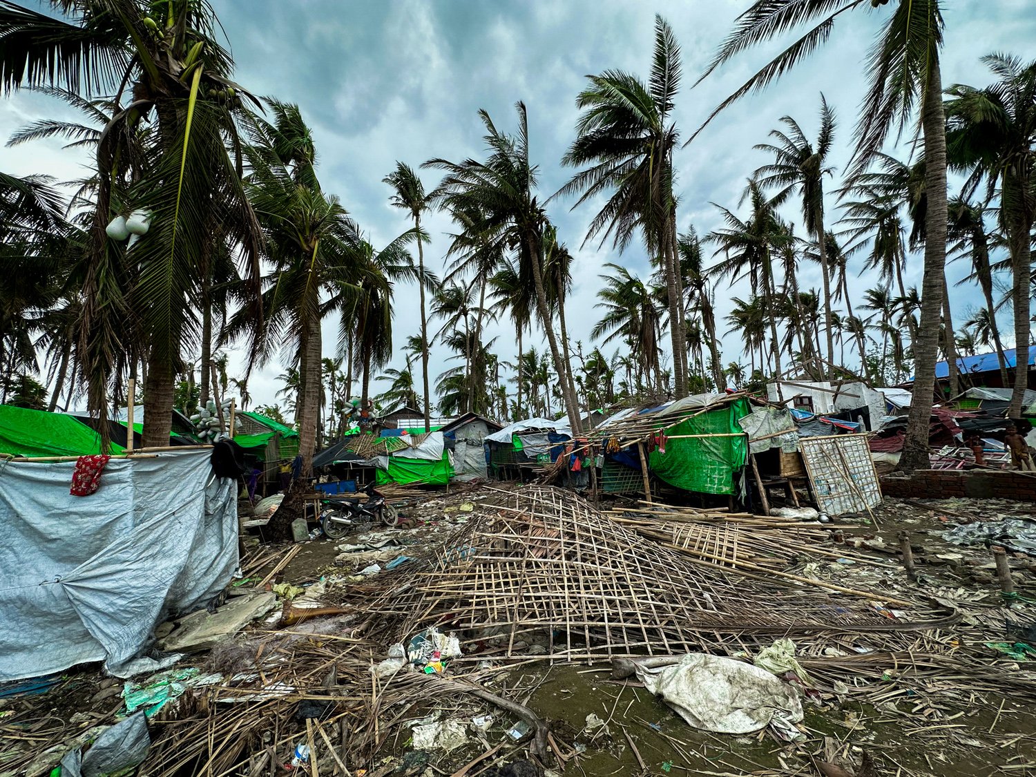 Makeshift shelters covered in tarpaulin dot a landscape littered with debris following a storm.