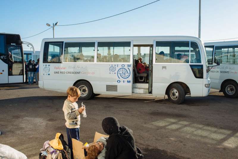A woman and her children wait to board the International Organization for Migration bus that will take them to their new shelter in Azraq camp.