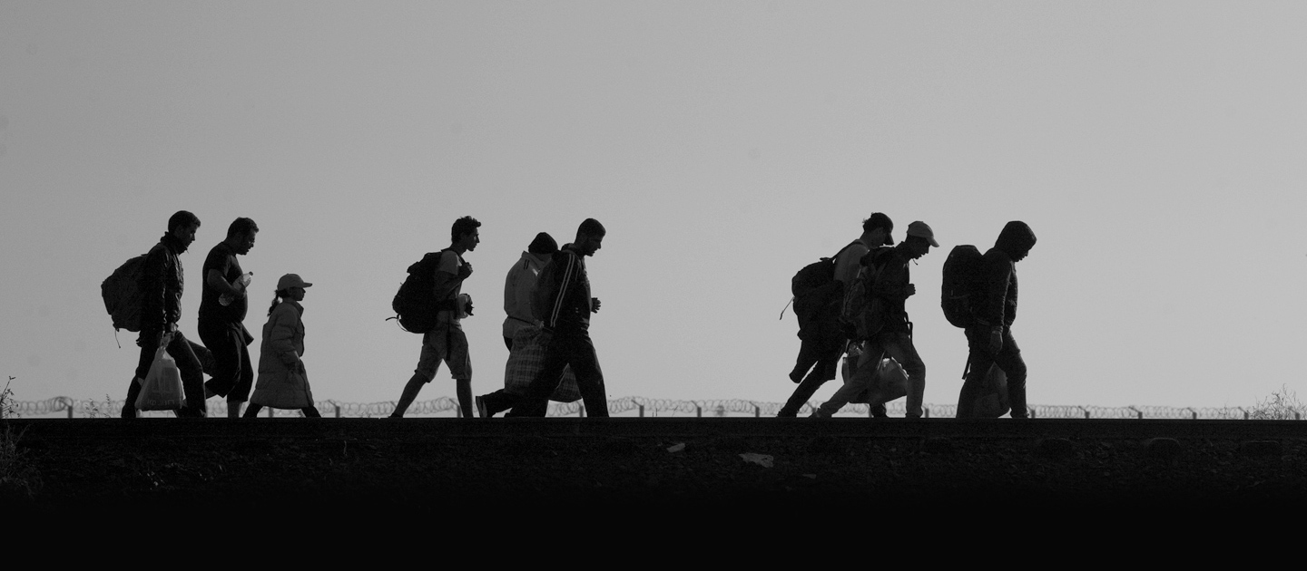 Photo : à l'horizon, la nuit, on voit les ombres de 9 personnes réfugiées qui marchent ensemble, portant des sacs sur leurs dos.