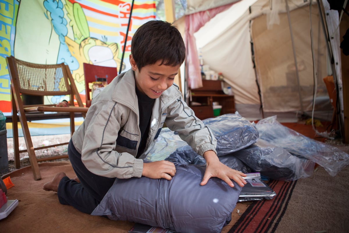 An Afghan boy opens a winter kit that will help him face harsh weather conditions in an open accommodation site