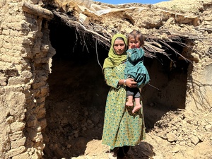 An Afghan IDP in front of her damaged house