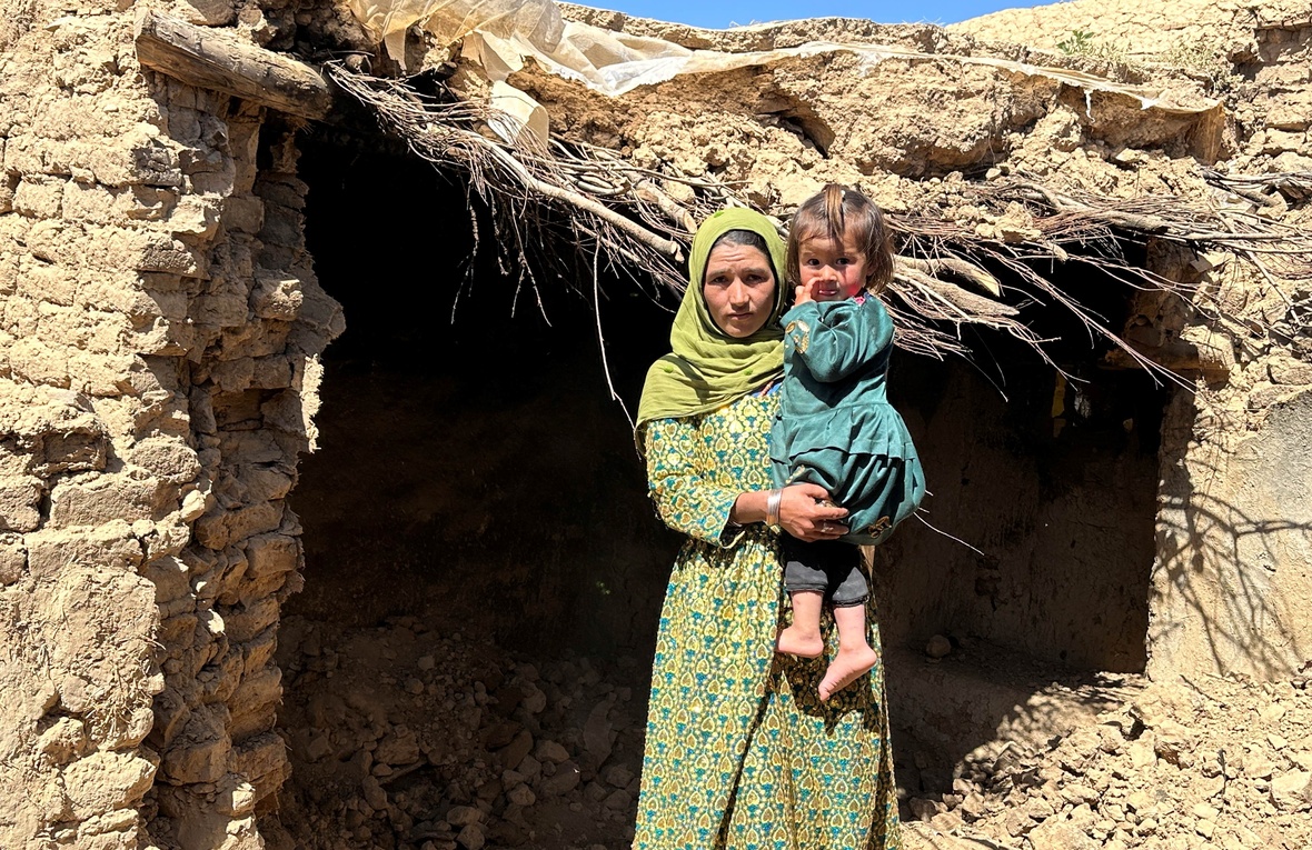 An Afghan IDP in front of her damaged house