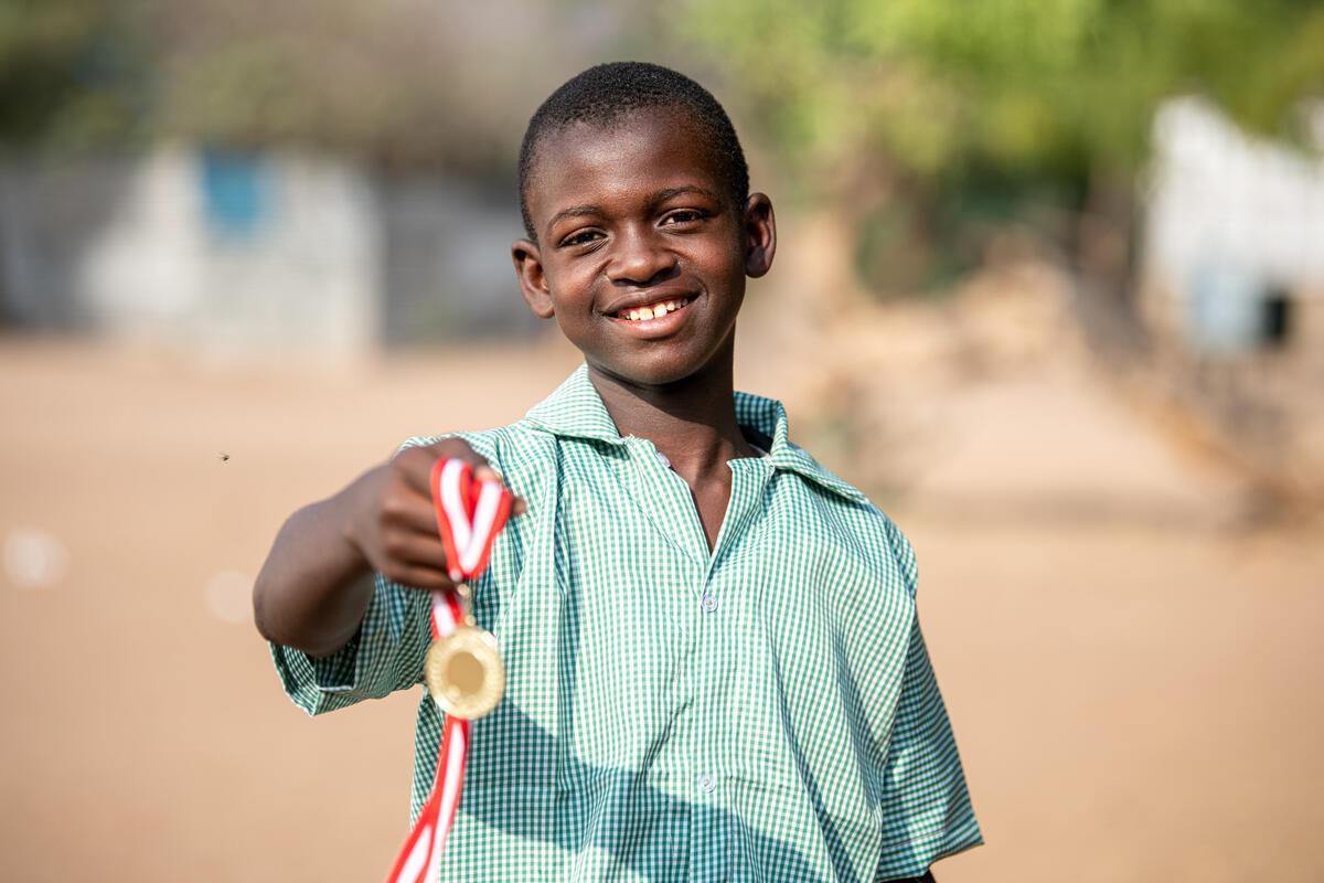 A 14-year-old Somalian boy poses outside, smiling and holding a medal