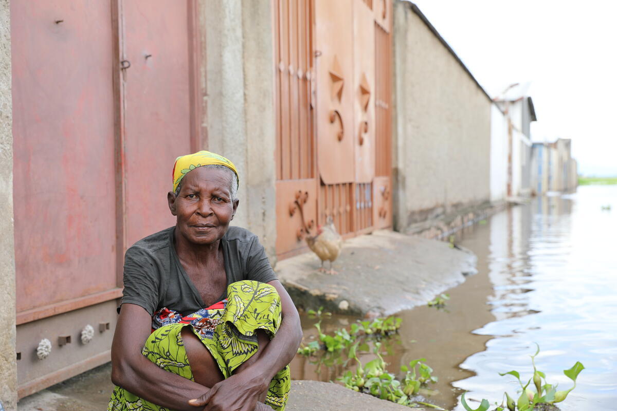 A woman sits on the ground in a flooded neighbourhood.