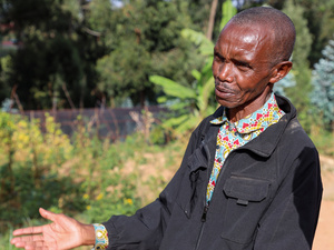 A man stands in front of a nursery of tree seedlings in a refugee camp.