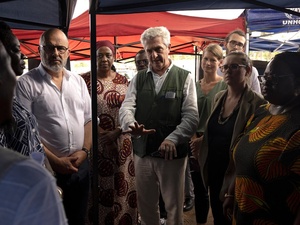A group of people meet outside under some colored shade cloth