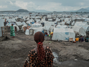 A rear view of a woman standing on muddy ground in front of hundreds of tents stretching to the horizon.