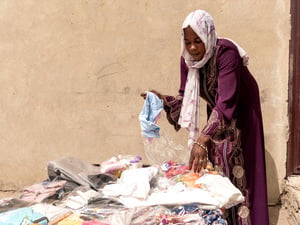 Halima sorting through new clothing items and everyday goods she sells in her shop that she opened after receiving a loan from a local Village Savings and Loans Association.