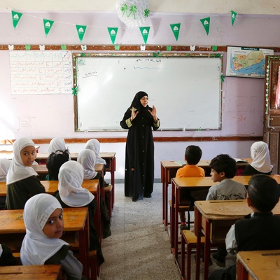 A teacher at the front of a classroom, with many students