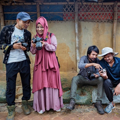 Four adults, two standing and two sitting, each examine a camera. 