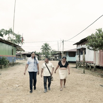 Three people walk together through a small village