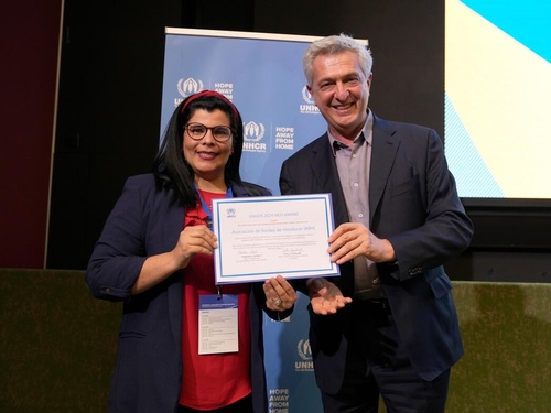 Ms. Estefani Claros Madrid and United Nations High Commissioner for Refugees Filippo Grandi holding up an award and smiling at the camera