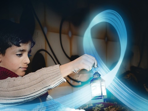 A young boy is holding a small lantern in a dark room. A blue, shiny and flying ribbon floats around the lantern.