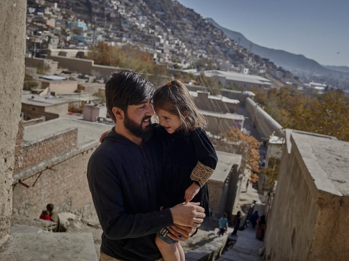 An internally displaced man in Afghanistan smiles as he hold his four-year-old daughter, the city of Kabul can seen in the background. 