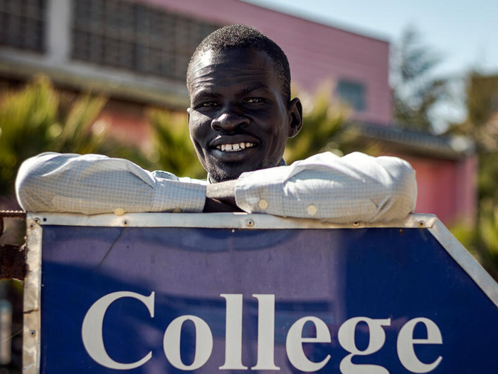 A young man poses, leaning against a sign that reads "College of law"