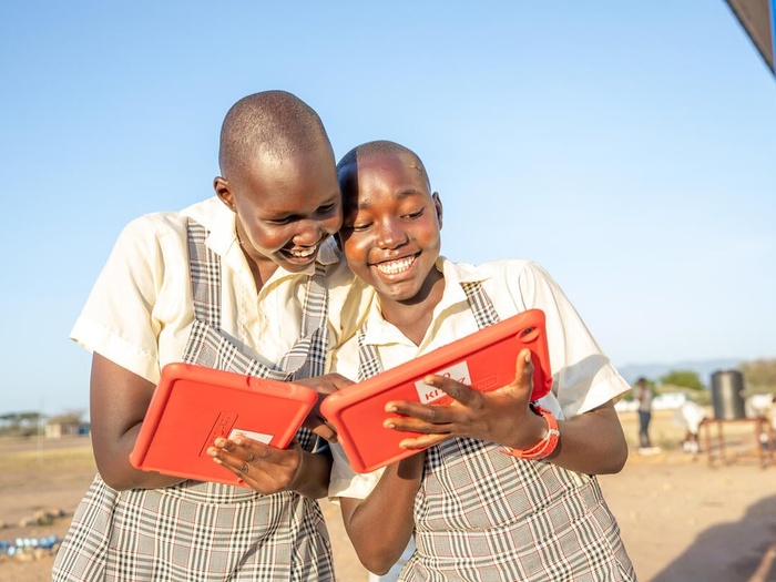 Two girls smiling as they use bright orange tablets.