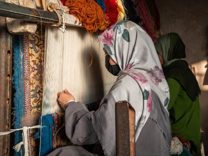 A woman weaving a carpet on a loom.