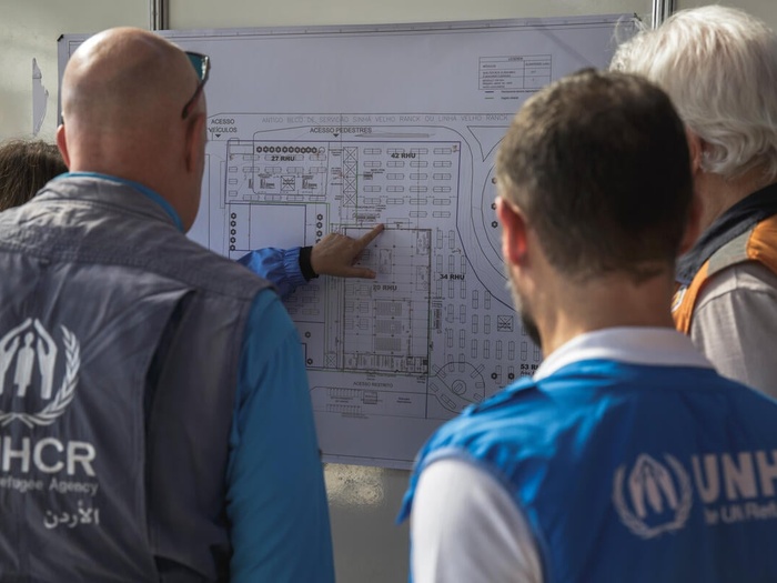 UNHCR staff look at a map of a shelter site on a whiteboard.