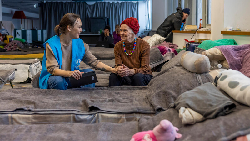 Une membre du personnel du HCR est assise sur un lit aux côtés d'une réfugiée et lui tient la main.