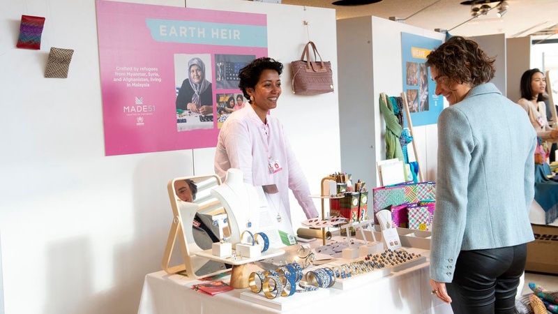 A woman browses jewelry and handicrafts at an indoor market stall.