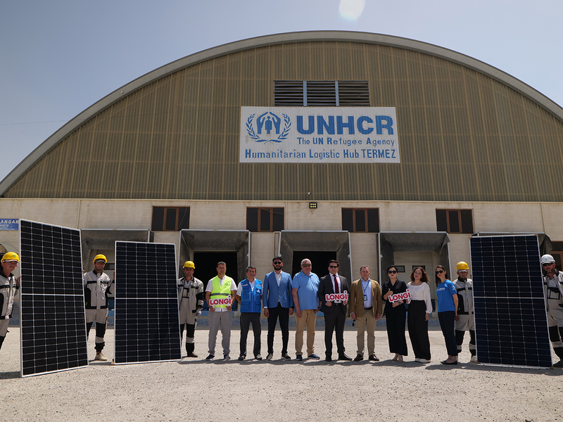 Fourteen staff from UNHCR and LONGi stand outside a large logistics hub, holding up several solar panels