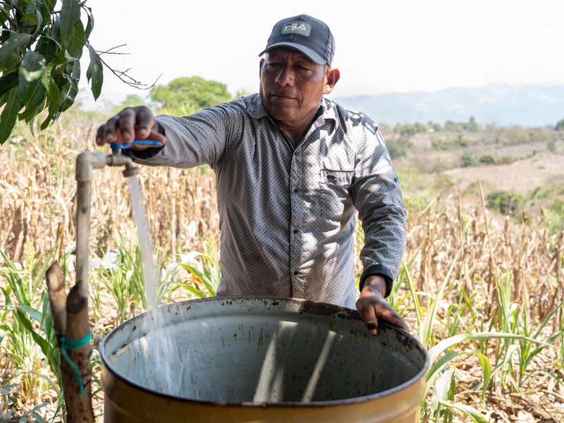 Salvadoran farmer José fills a metal drum with water on his farm.