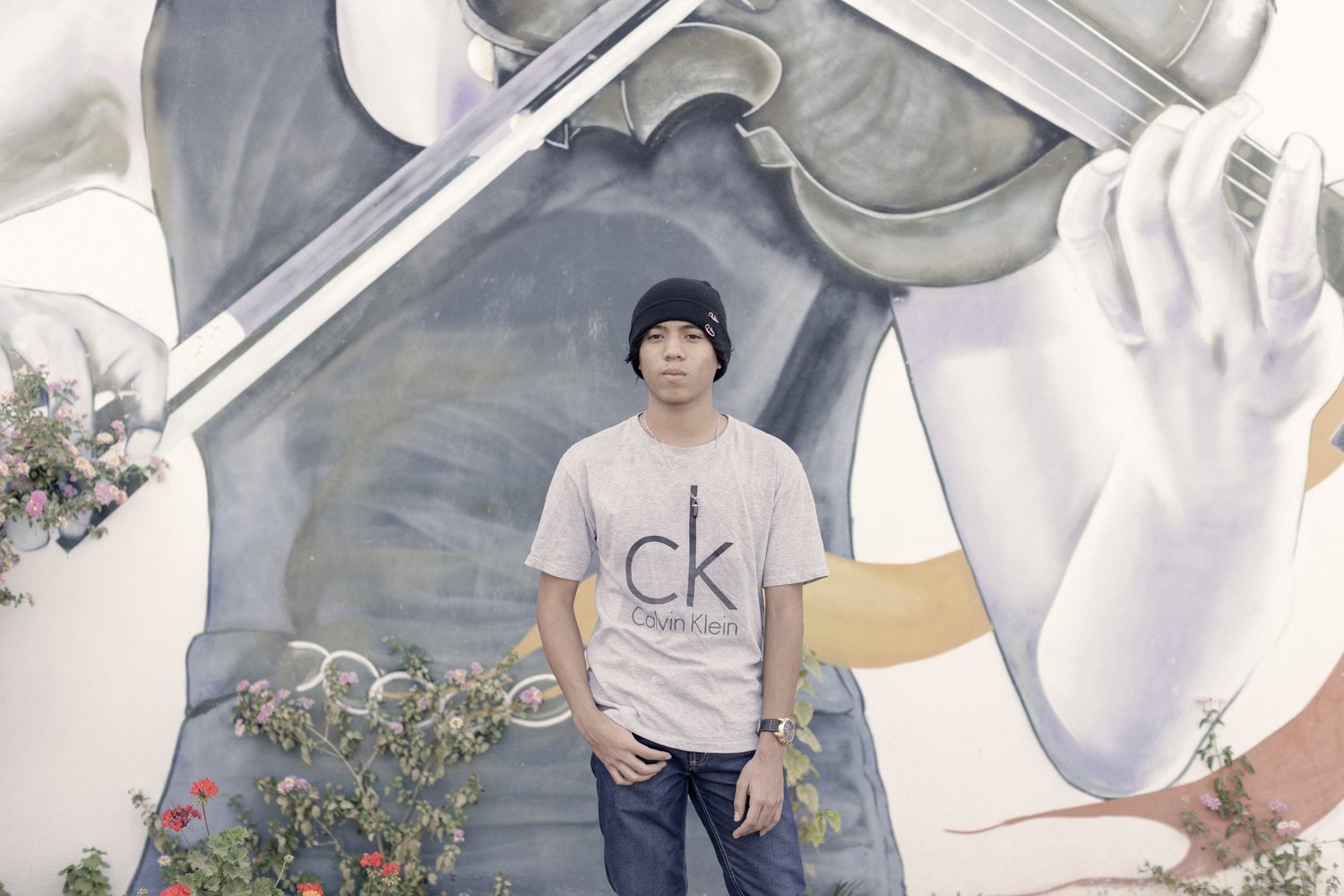 A young man stands in front of a mural of someone playing the violin.