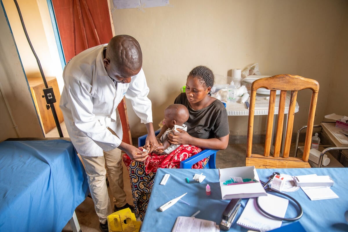 A mother holds her child as a doctor takes blood sample at a medical centre.