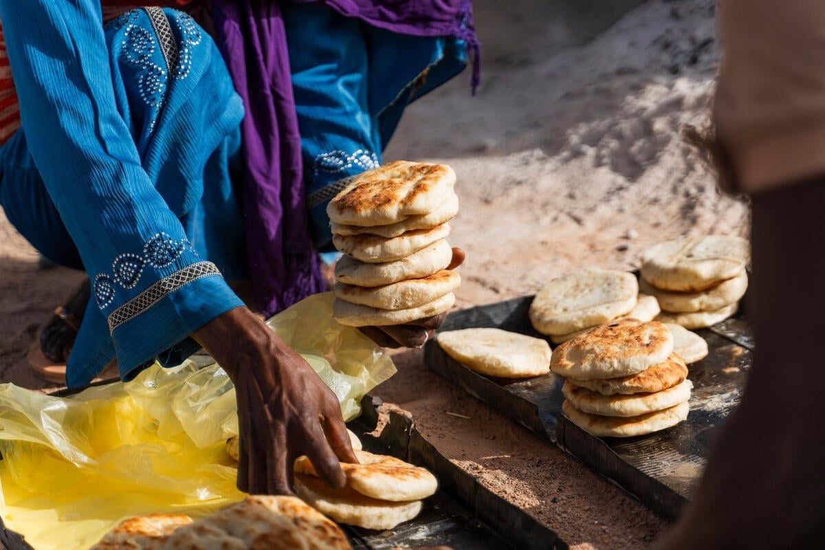 A woman picks up small rounds of bread to sell to a customer.