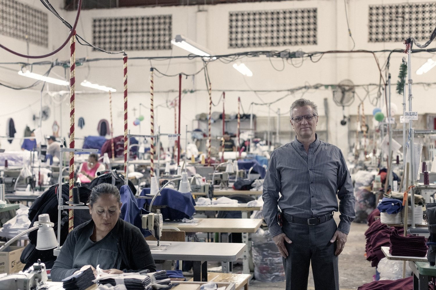 A man stands on a factory floor where women are at work using sewing machines.