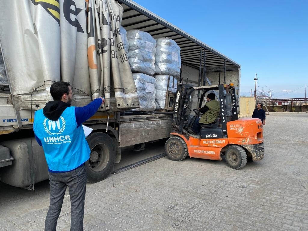 A forklift truck removes relief items from the back of truck under the direction of a UNHCR staff member.