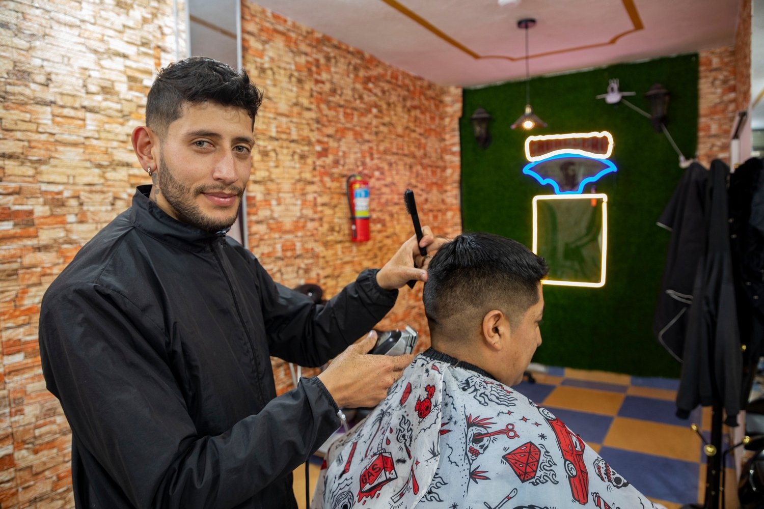 A barber pauses cutting a client's hair to look at the camera.