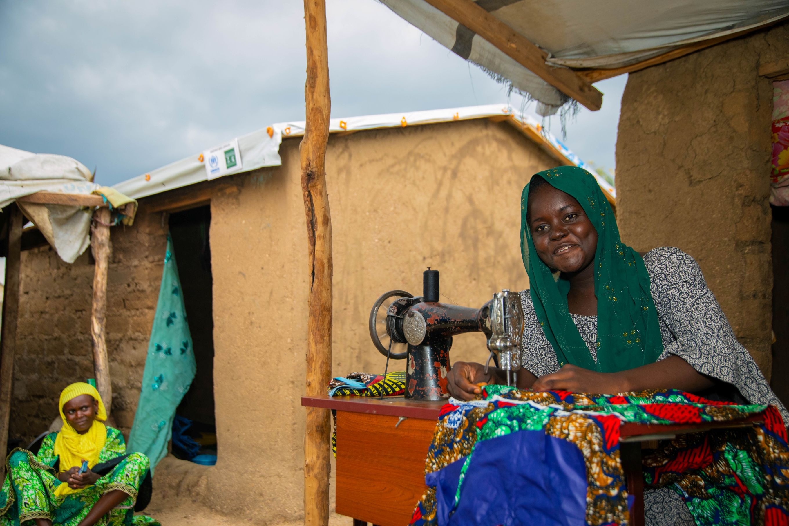 Nigerian refugee, Falmata Mohammed sews outside their house with a new roof in Minawao.