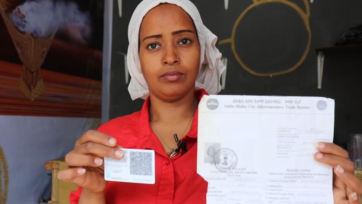 A woman wearing a red short holds up an ID card in one hand and a printed piece of paper in the other