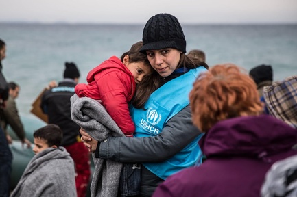 A UNHCR staff member holds a young refugee child in a blanket.