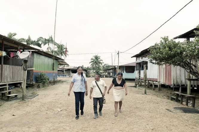 Three people walk together through a small village