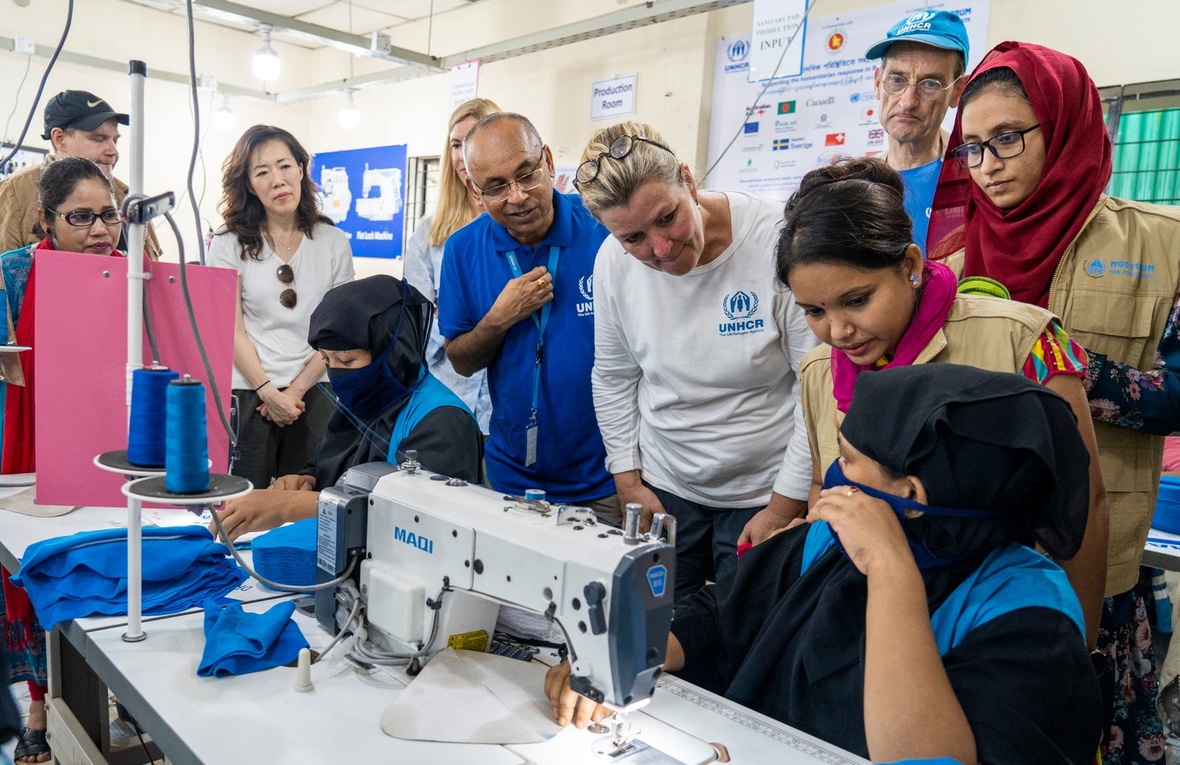 A group of people talk to a woman sitting at a sewing machine.