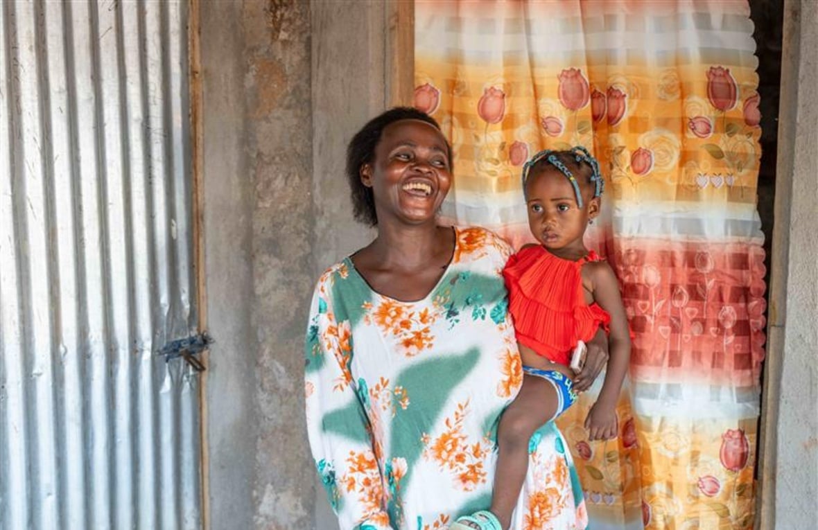 Sofia, a refugee mother from the Democratic Republic of Congo, stands outside the shelter she built with support from UNHCR, holding her two-year-old daughter, Apolina. Sofia is happy to have a place they can call home. 