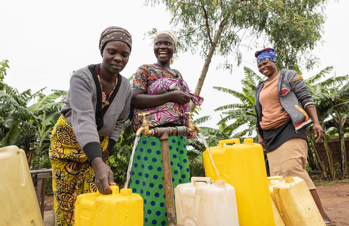 Nikuze Rachel (left) and her neighbours Tumusifu Marcelina  and Shimiyimana Charlotte collect water at a water point in her neighbourhood in Rubondo, Nakivale refugee settlement. As a water user committee member, she helps to protect and care for the community water source.