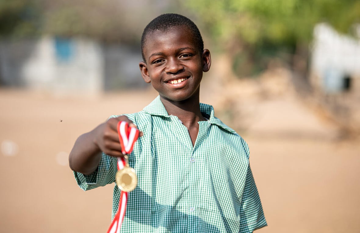 A 14-year-old Somalian boy poses outside, smiling and holding a medal