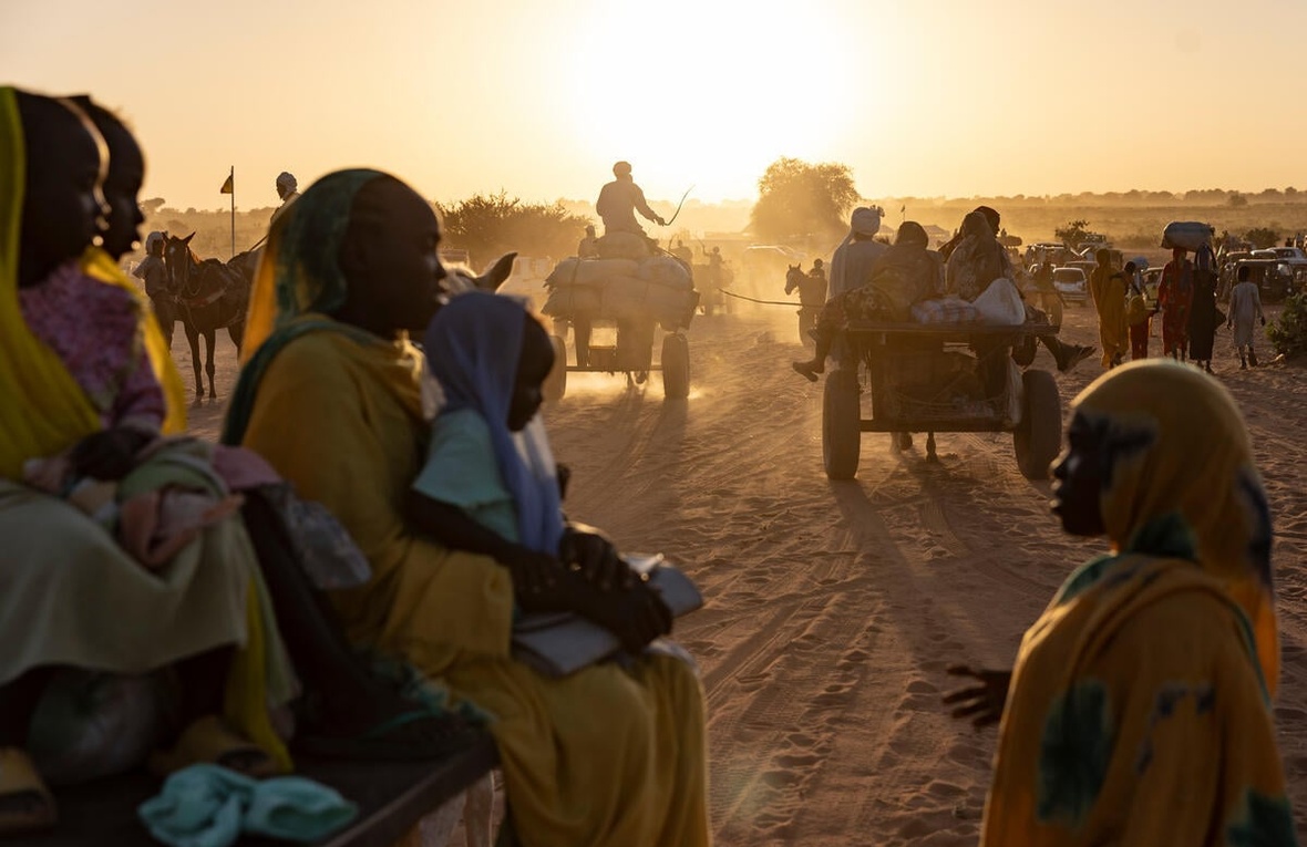 The sun lights up the dust behind groups of Sudanese refugees walking and on carts behind horses