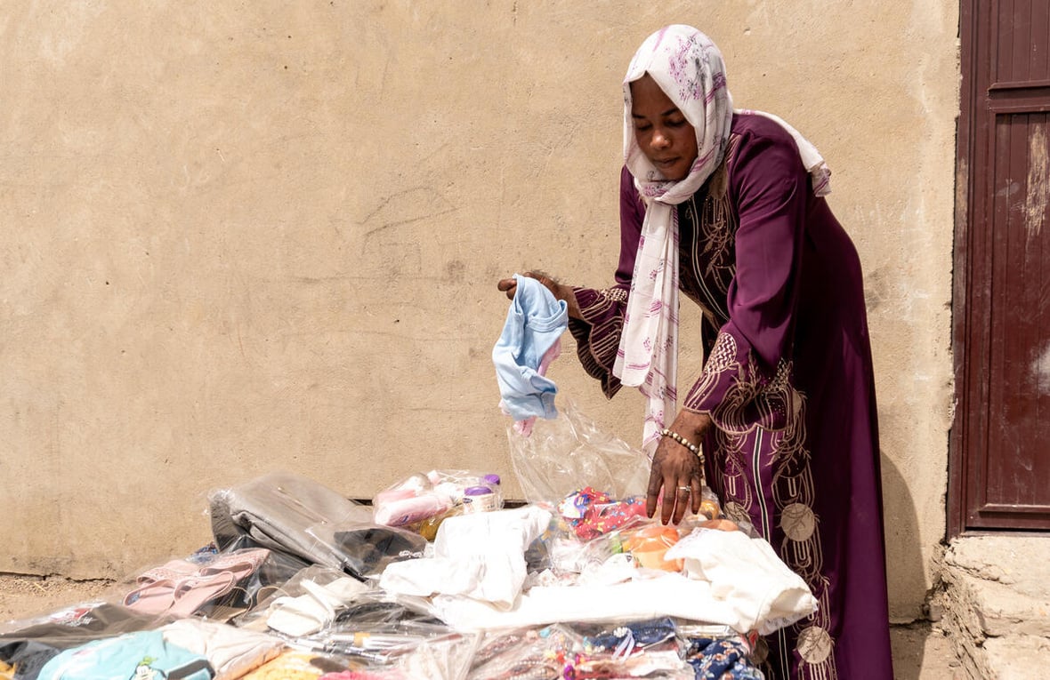 Halima sorting through new clothing items and everyday goods she sells in her shop that she opened after receiving a loan from a local Village Savings and Loans Association.