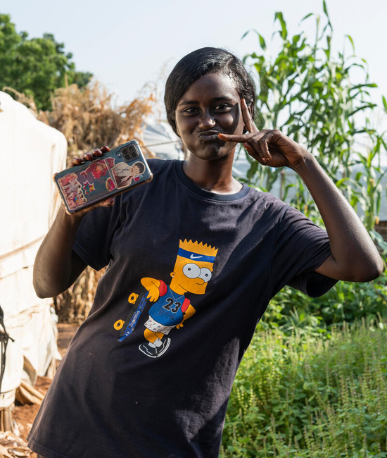 A young woman poses for a photo while holding up her phone