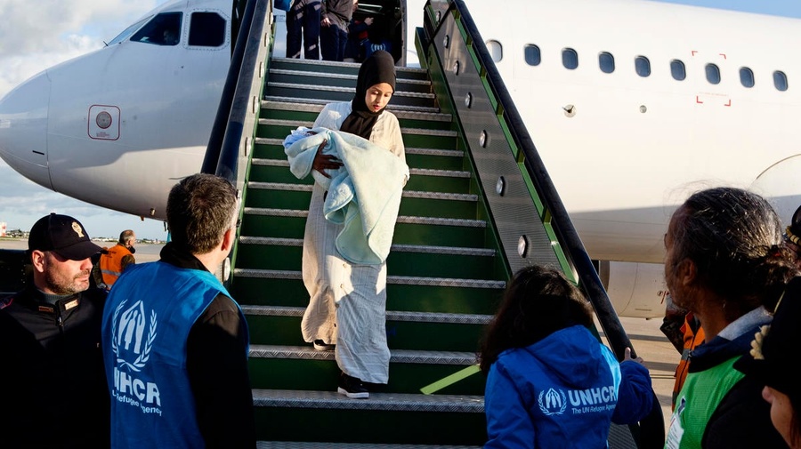 A Somali woman holding a baby is greeted by UNHCR staff as she exits a plane after being evacuated from Libya to Italy. 