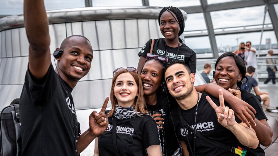 A group of young people in UNHCR t-shirts take a selfie. 