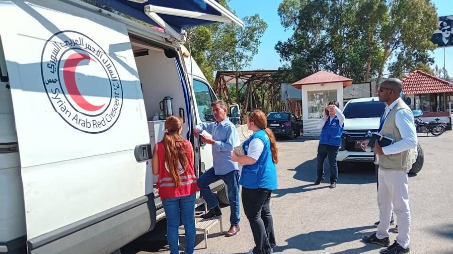 UNHCR and Syrian Arab Red Crescent staff converse outside a large Syrian Arab Red Crescent van with an open door