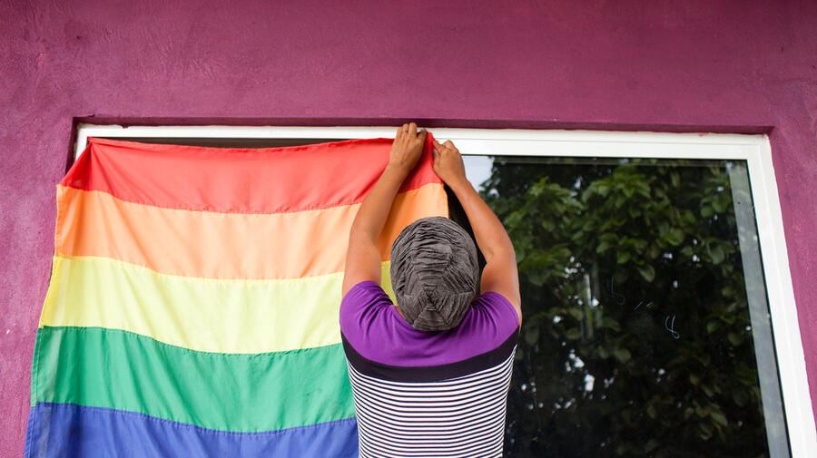 A person hangs a rainbow flag to a window.