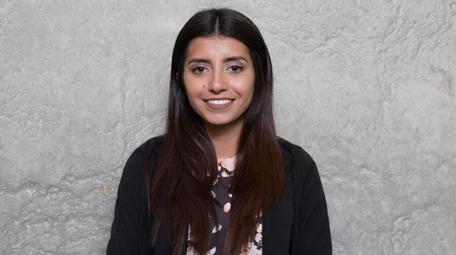 Portrait of a young woman standing against a grey background.