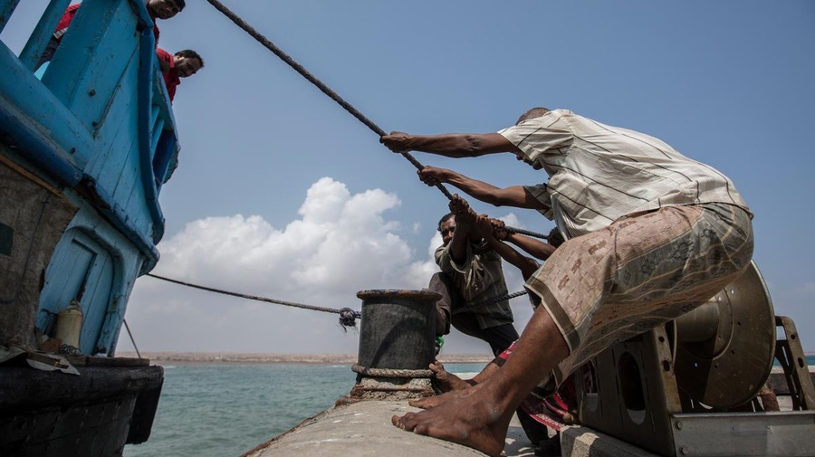 Men pull a rope to bring a boat into dock.