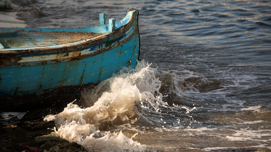 Waves crash against the bow of a teal fishing boat 